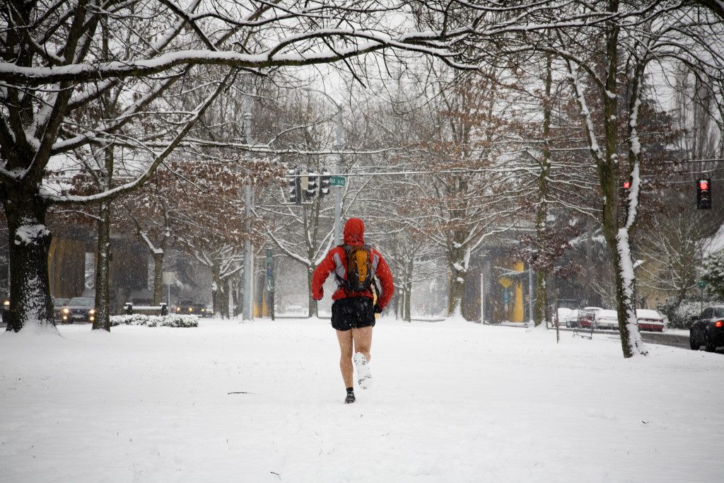A male runner with a backpack runs down a city street while wearing shorts in the winter.