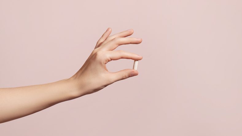 Hand holding the supplements on pink background
